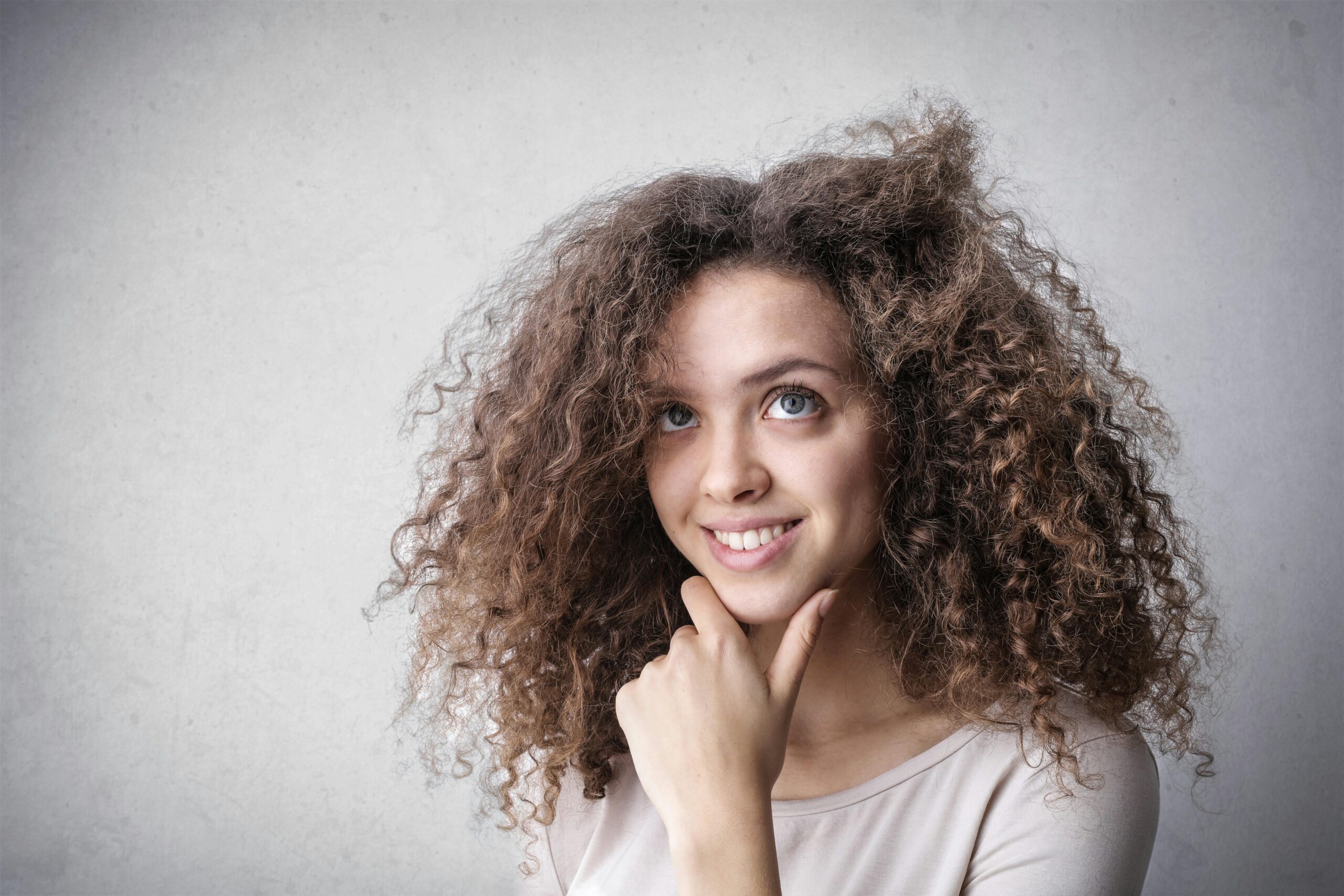 Smiling young woman with curly hair in a studio portrait setting.