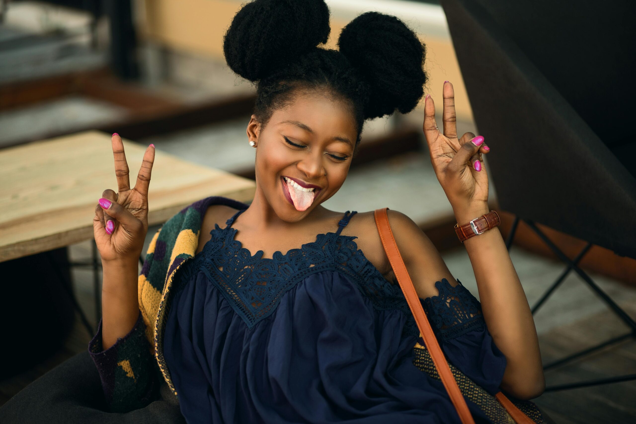 Joyful young woman making peace signs and posing playfully indoors.