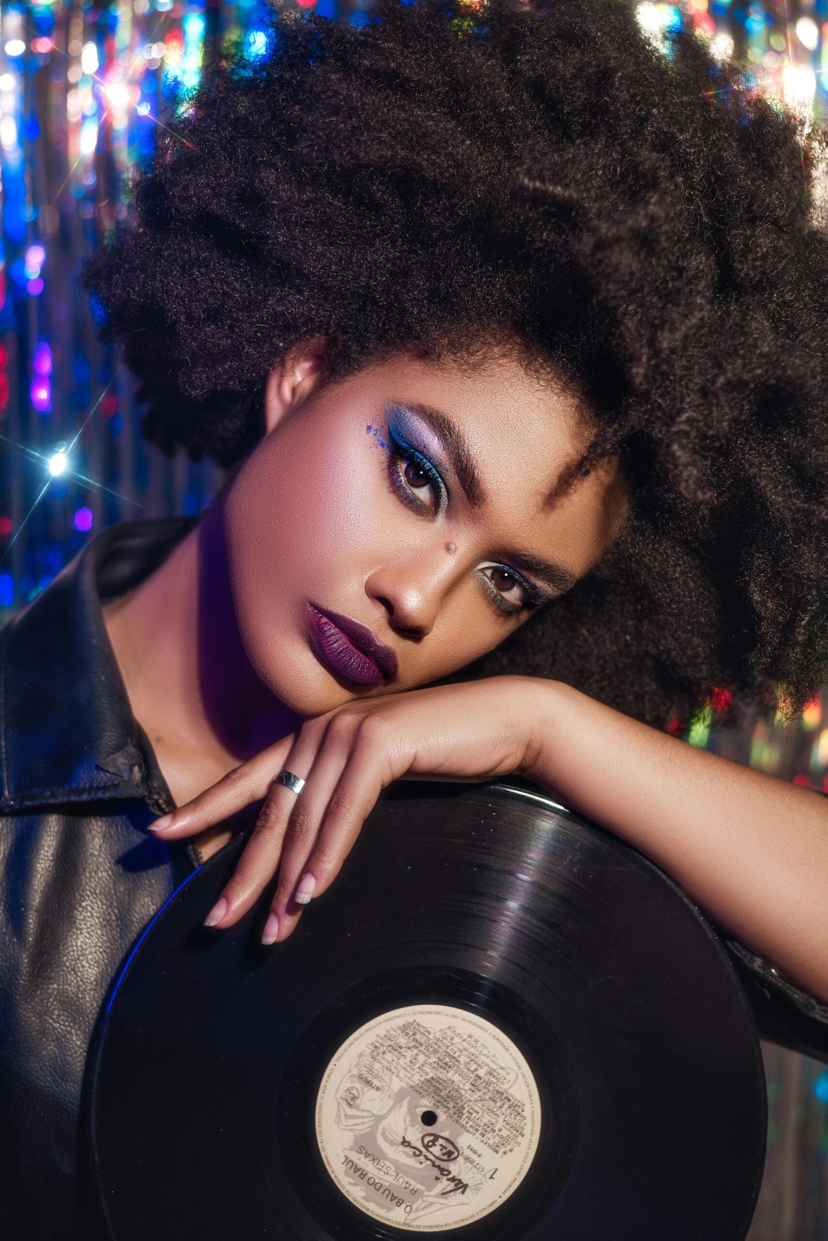 Stylish woman with afro holding a vinyl record in a vibrant studio setting.