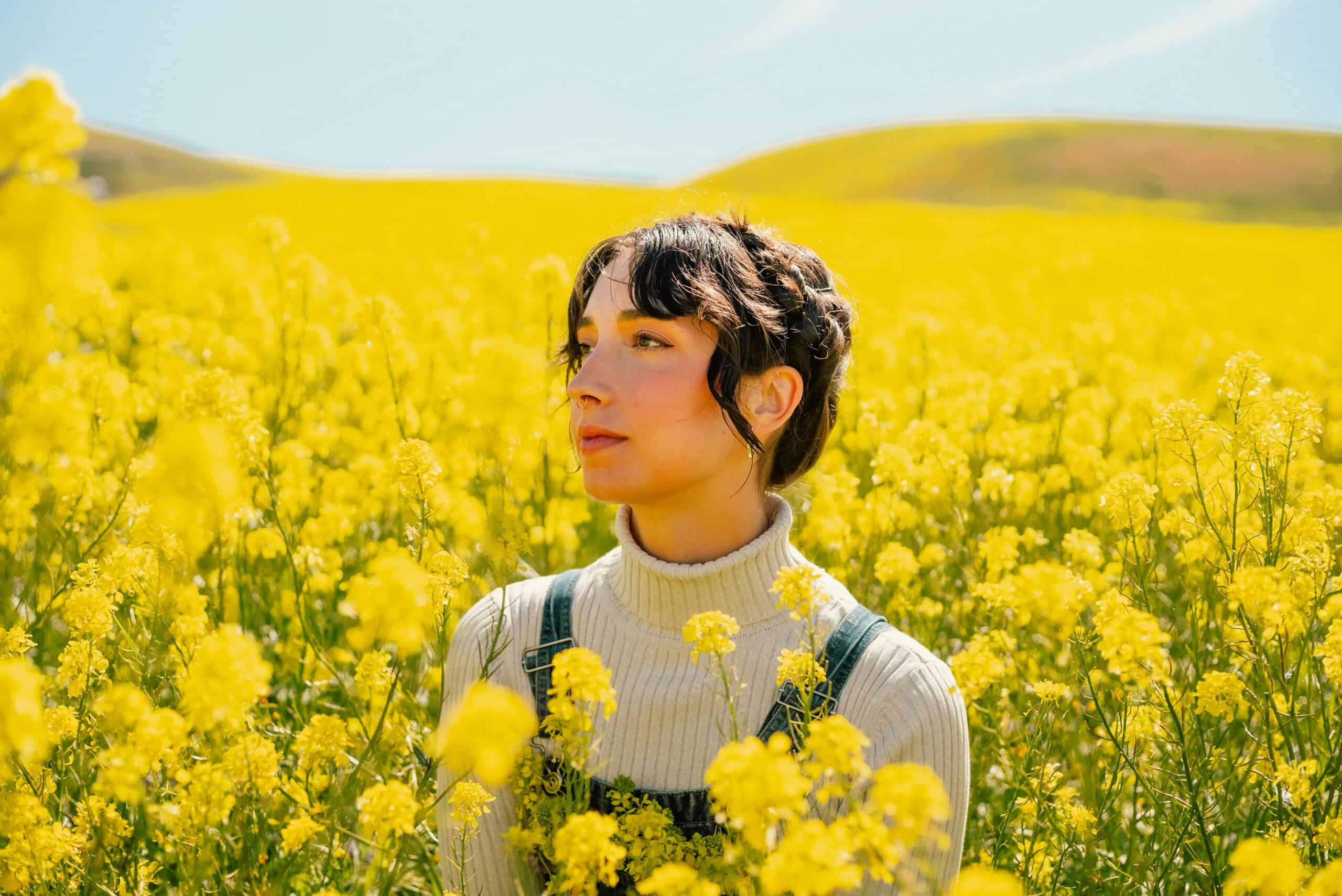 Portrait of a woman surrounded by vibrant yellow flowers in a spring field.