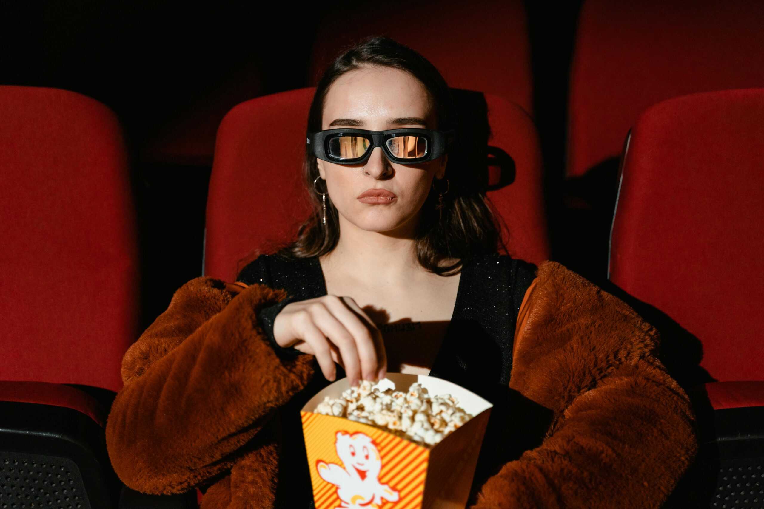 A woman in a fur coat enjoying popcorn while watching a 3D movie in a cinema.