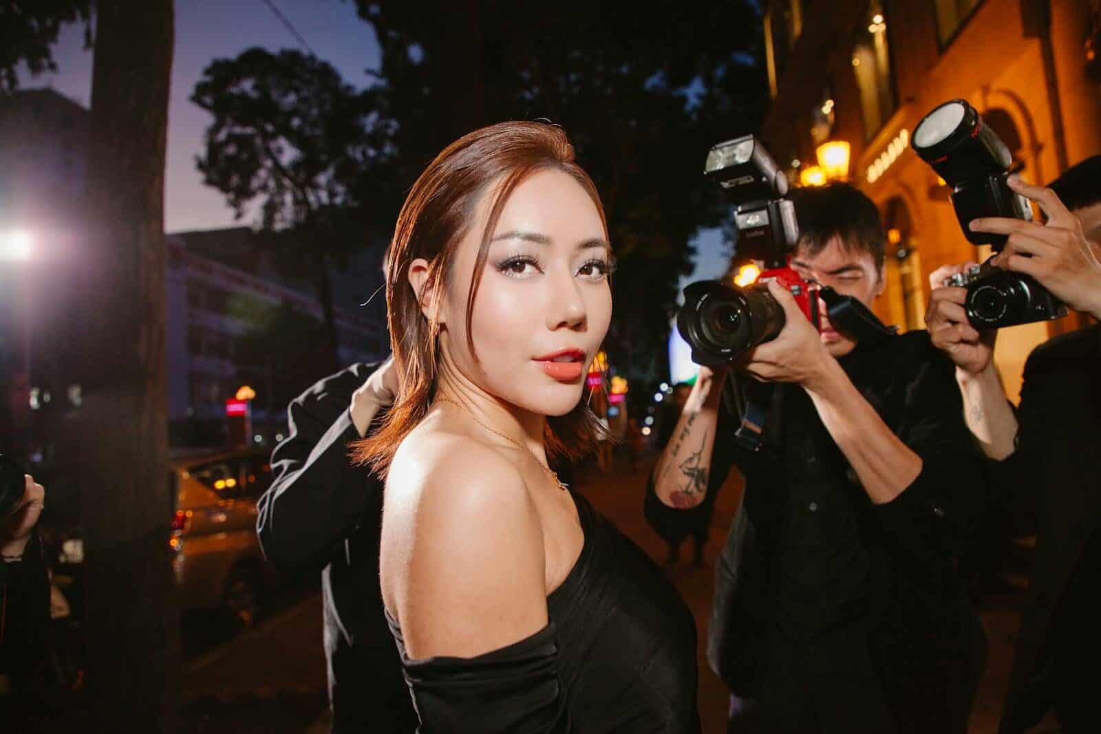 A glamorous woman in black poses confidently for photographers at a night event.