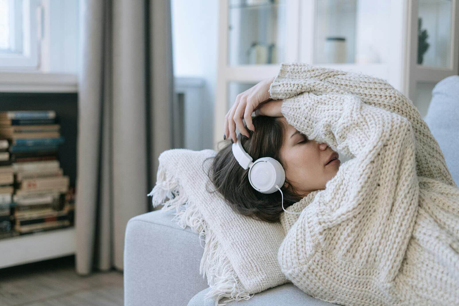 A young woman in a knitted sweater relaxing with headphones, conveying a sense of calm and introspection.