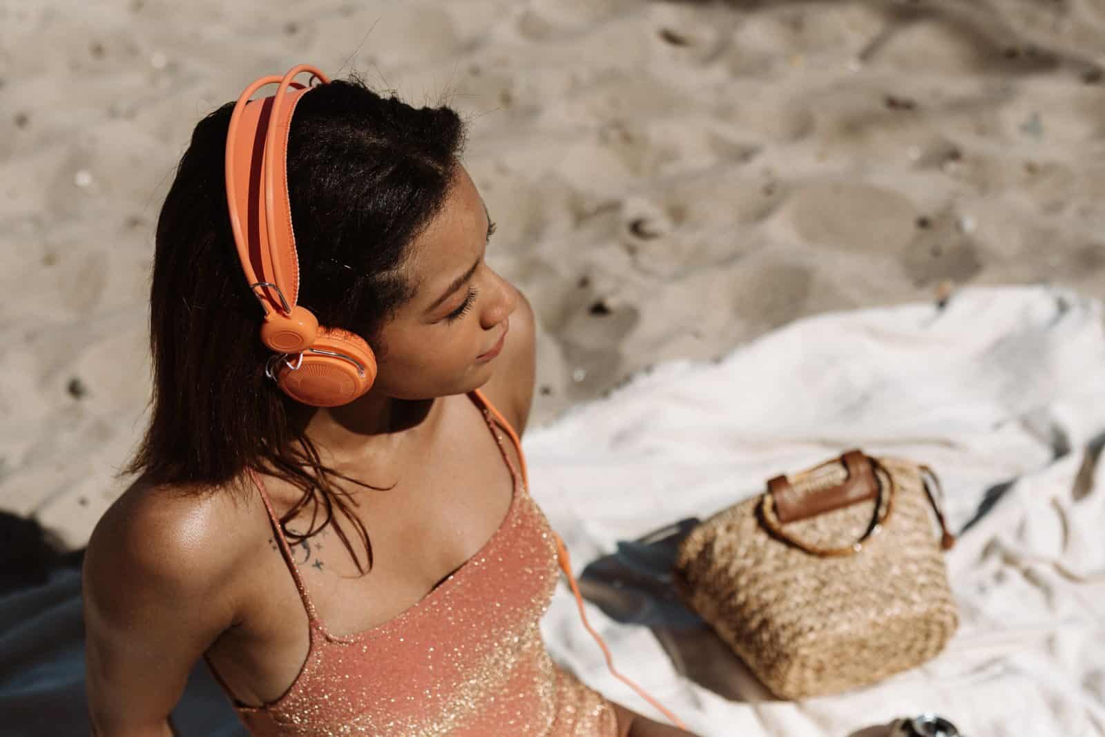 A young woman relaxes on the beach wearing headphones, enjoying the sun and music.